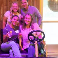 Four event attendees smiling at camera, two sitting in mini-golf cart